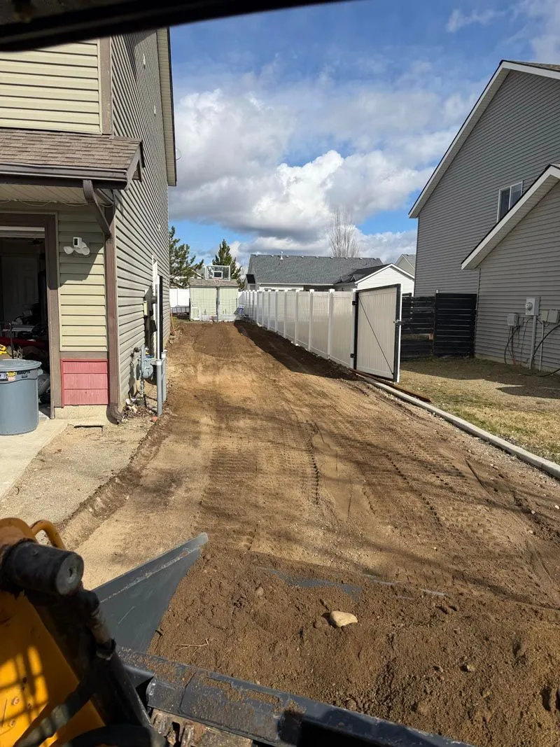 Skid steer leveling dirt for a side-yard driveway between two houses