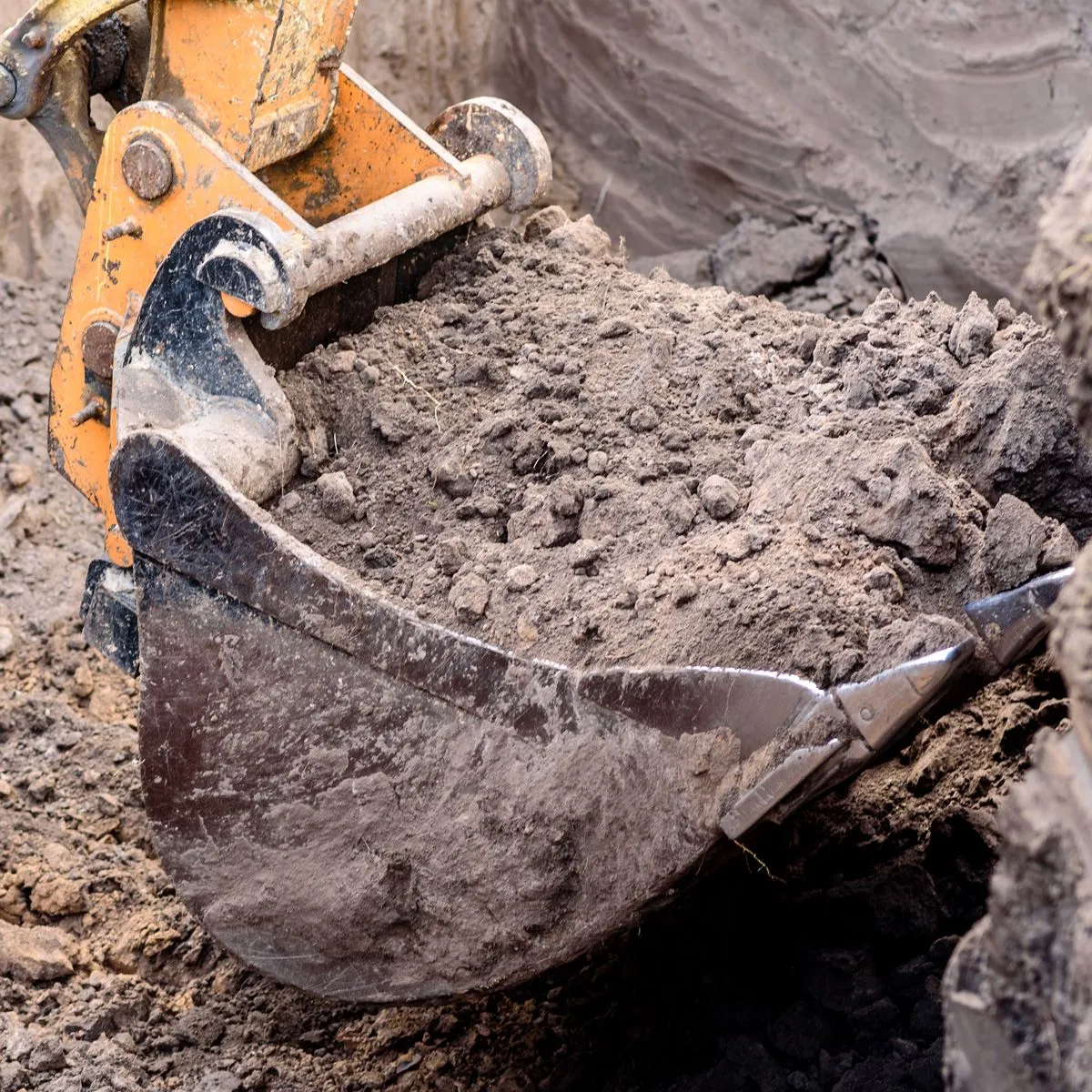 Excavator bucket scooping loose soil on a job site