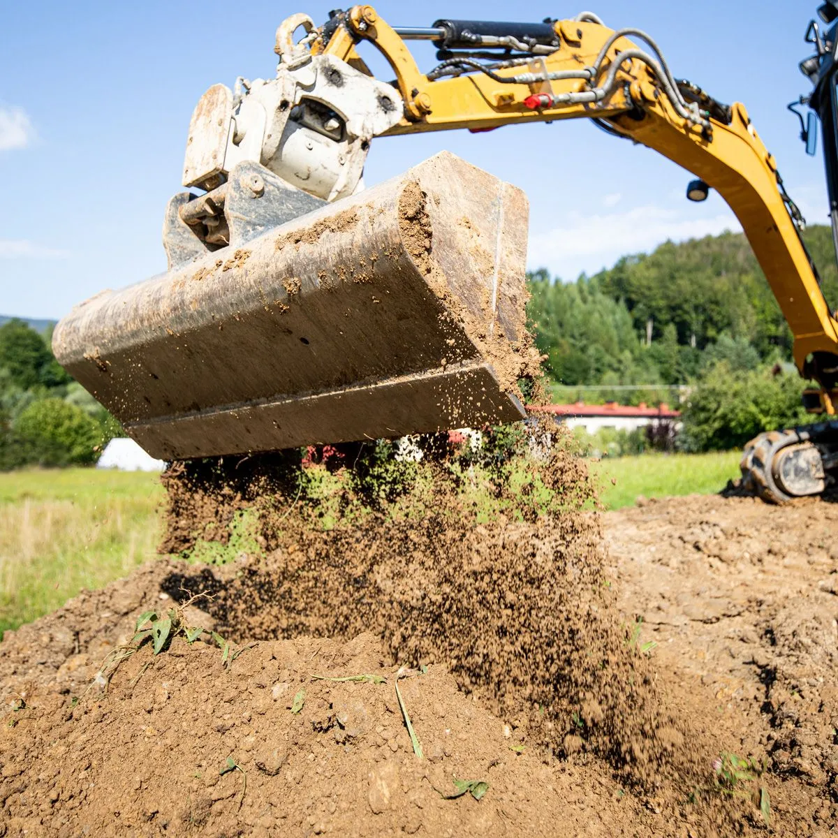 Excavator lifting a full bucket of dirt and roots while clearing land