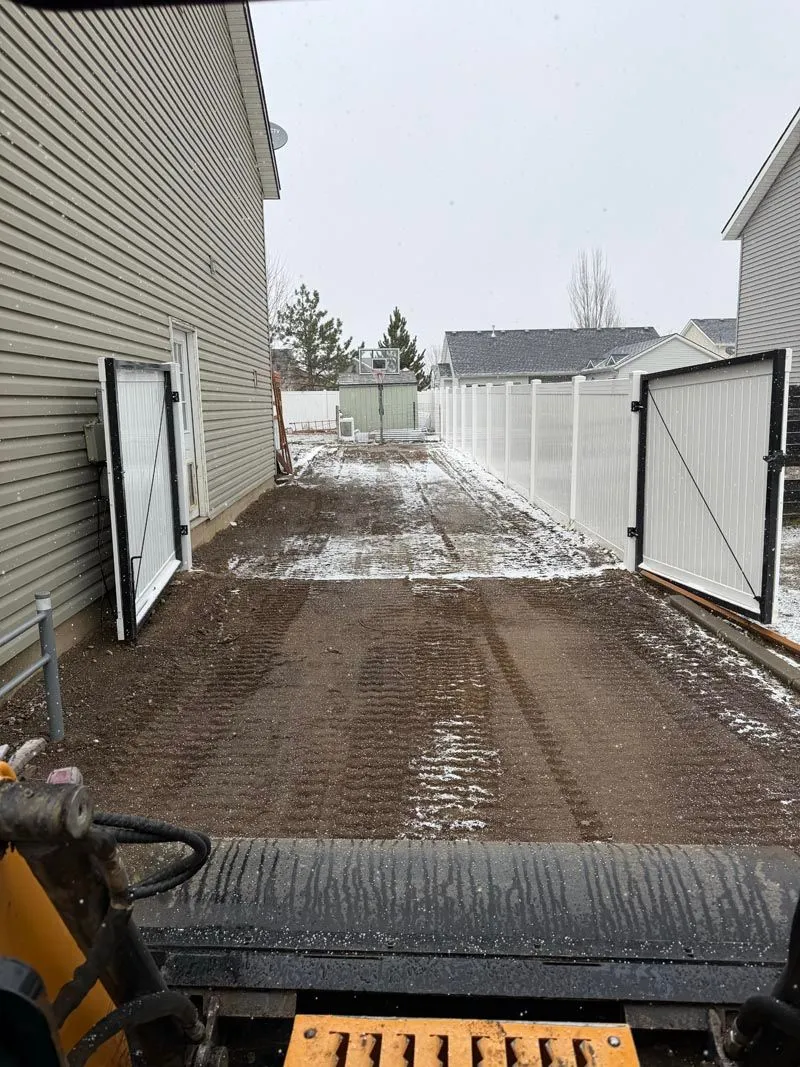 Side-yard driveway power-raked in early winter, viewed from the skid steer