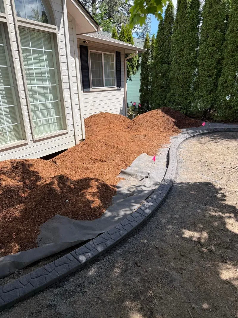 Bark mulch bed and drainage prep along the side of a house